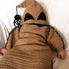 a baby wrapped in a crocheted blanket laying on top of a bed