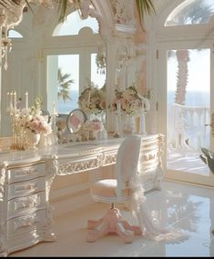 an ornate white desk and chair in a room with large windows overlooking the ocean is adorned with pink flowers