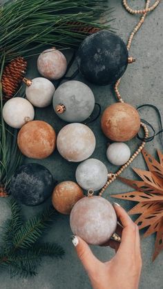 a person is holding some balls in front of pine branches and other ornaments on the ground