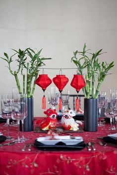 the table is set with black and red plates, silverware, vases, and bamboo plants