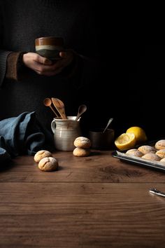 a person holding a cup over a table with pastries and lemons on it