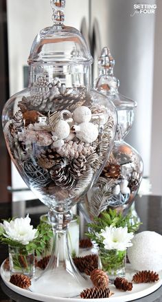 two glass vases filled with pine cones and other decorations