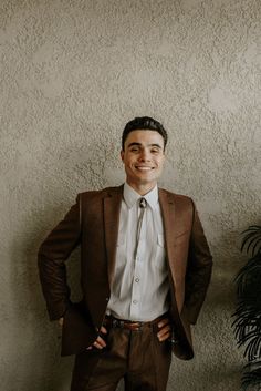 a man wearing a suit and tie standing in front of a wall