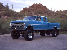 a blue truck parked on top of a parking lot next to a cactus covered hill