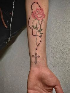 a person with a rose tattoo on their arm holding a rosary and cross in the other hand