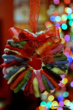 a multicolored wreath hanging from a christmas tree with lights in the back ground