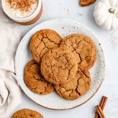 a white plate topped with cookies next to cinnamon sticks and two mugs of coffee