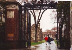 people walking under an iron gate on a rainy day in front of a brick building