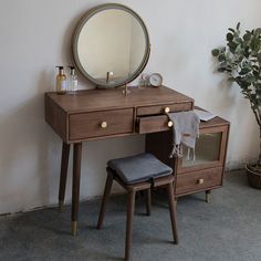 a dressing table with a mirror and stool next to a potted plant on the floor