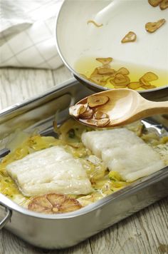 a pan filled with fish and vegetables on top of a wooden table next to a spoon