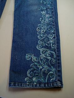 a pair of blue jeans with an embroidered design on the bottom and side, sitting on a table