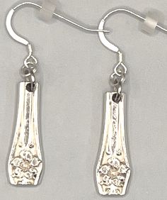 two silver earrings are hanging from hooks on a white surface, one has an ornate design and the other is small