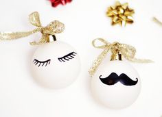 two christmas ornaments with fake eyelashes and a moustache drawn on one ornament