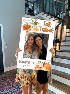 two women standing next to each other in front of stairs holding up a photo frame