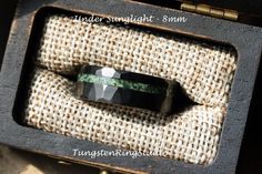 a black and green ring sitting on top of a piece of cloth in a box