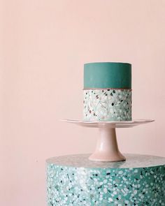 a three tiered cake with blue and white frosting on a table next to a pink wall