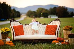 a baby sitting on top of a couch surrounded by pumpkins