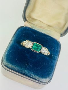 an antique emerald and diamond ring in a velvet box with blue velvet lining the edges