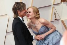 two people standing next to each other in front of an oscars red carpet with one person wearing a tuxedo