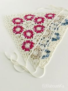 a piece of white crocheted material with red, blue and pink flowers on it