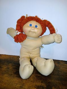 a small doll with red hair and blue eyes sitting on top of a wooden table