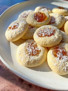 powdered sugar covered cookies on a white plate with jam in the middle and jelly filling