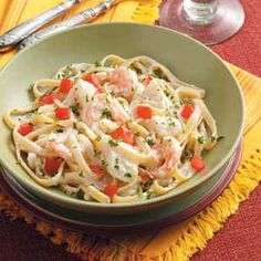 a bowl of pasta with shrimp and carrots on a yellow placemat next to silverware