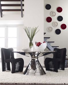 a glass table with black chairs and plates on it in front of a wall decorated with circles