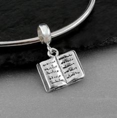 "This Book Charm comes with a silver dangle bead as pictured.  Fits on all major brand European style bracelets. A list of compatible chains is available here: https://etsy.me/2BY7DAW { DETAILS } ★ Charm Metal: 925 Sterling Silver ★ Bead Metal: Stainless Steel ★ Finish Color: Silver ★ Charm Size: 3/8\" x 1/2\" ★ Style: 3-Dimensional ★ Attachment: 5mm diameter large hole bead ★ Available without bead attached upon request Photo is not to scale and may appear larger to show detail.  Refer to exact Pandora Bracelet Designs, Book Charm, Writer Gifts, Pandora Beads, Large Hole Beads, Open Book, Silver Bead, Gift Jewelry, Dangle Charms