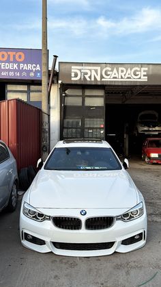 a white car parked in front of a garage with two other cars behind it on the street