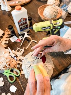 a person cutting out paper on top of a wooden table with scissors and other crafting supplies