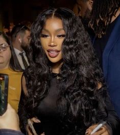 a woman with long black hair standing in front of a group of people holding cell phones