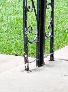 an iron gate with a clock on it in front of a grassy field and sidewalk