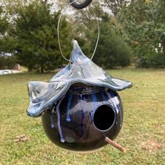 a blue birdhouse hanging from a wire in the grass with trees in the background