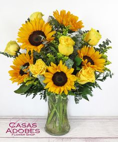 a vase filled with yellow sunflowers on top of a wooden table next to a white wall