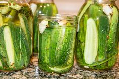 three jars filled with cucumbers sitting on top of a granite counter next to each other