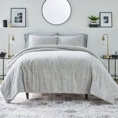 a bedroom with white walls and a round mirror on the wall above it, along with a bed covered in grey linens