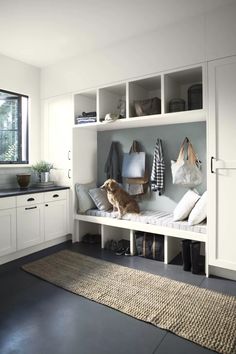 a dog is sitting on a bench in the middle of a room with white cabinets