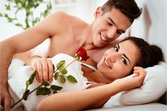 a man and woman laying in bed with one holding a rose, the other smiling