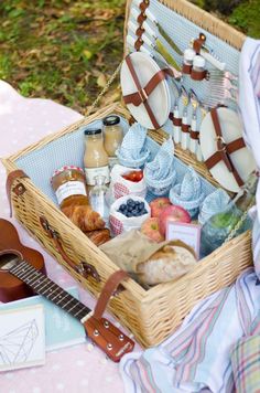 a picnic basket filled with food on top of a pink cloth covered table next to a guitar