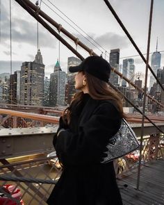 a woman standing on top of a bridge next to a tall cityscape with buildings in the background