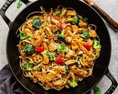 a skillet filled with noodles, broccoli and chicken on top of a table