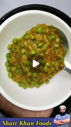 a white bowl filled with green peas on top of a black and white plate next to a man's hand