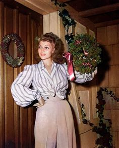 a woman is standing in front of a wooden wall with wreaths on the door