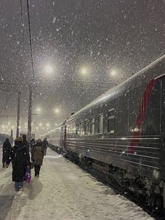 people are walking on the snow covered sidewalk next to a train