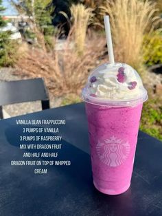 a pink starbucks drink with whipped cream on top sits on a table in front of some grass