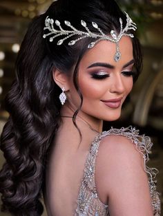 a woman with long hair wearing a tiara and makeup looks down at her shoulder