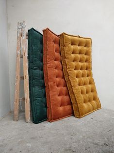 three different colored cushions sitting next to each other on top of a cement floor in front of a white wall