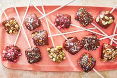 there are many chocolates on the pink tray with white sticks in them and sprinkles