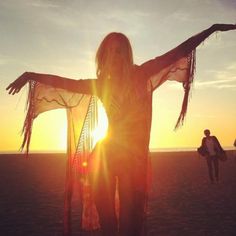 a woman standing on top of a beach next to the ocean with her arms outstretched